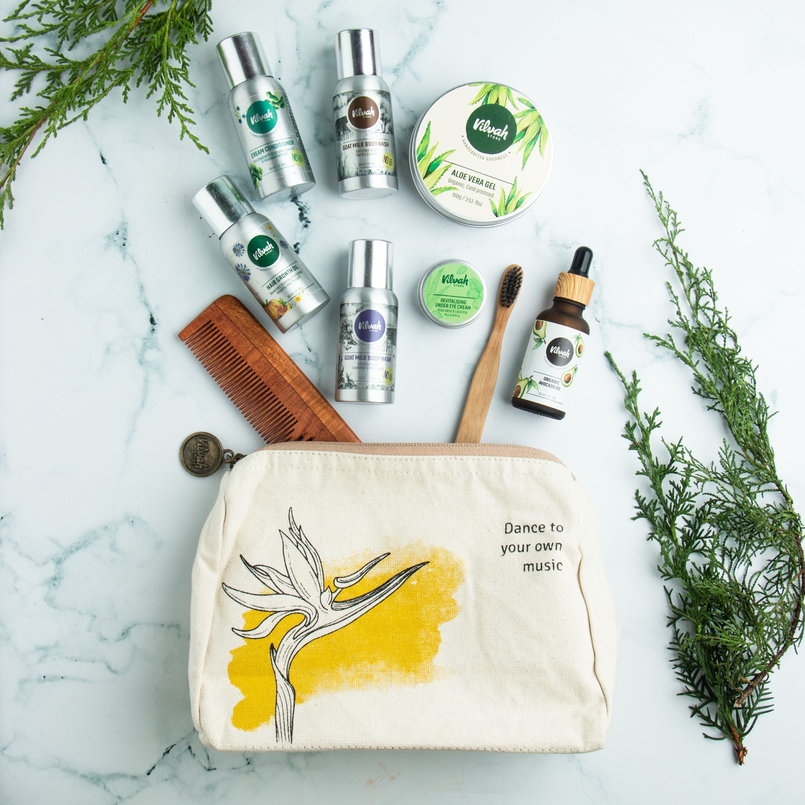 Flat lay of various natural cosmetics with canvas bag and greenery on a marble background.