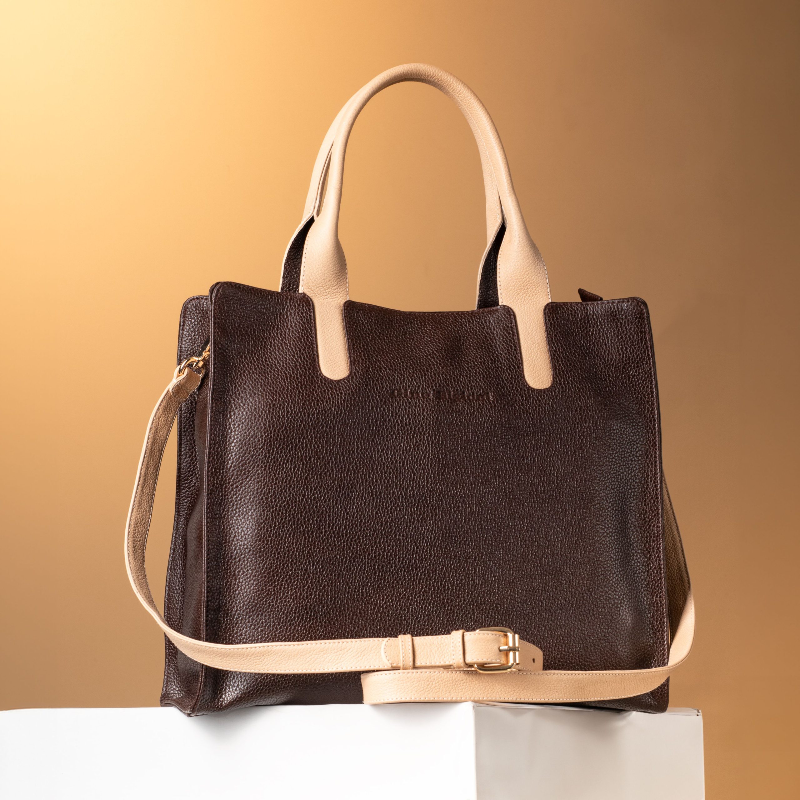 Luxury dark brown leather handbag with beige handles and strap, exuding fashion elegance.